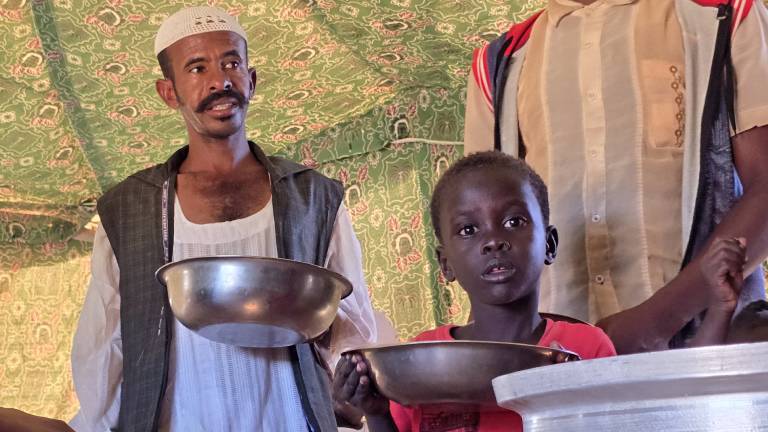Ein Mann und ein Kind stehen mit Schüsseln in der Hand an einer Essensausgabe (Meroë/Sudan, 09.01.2025)