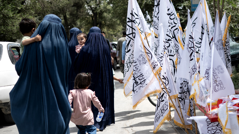 Afghanische Frauen in Burkas gehen am Vorabend des vierten Jahrestags der Machtübernahme der Taliban im Jahr 2021 an Taliban-Flaggen vorbei, in Kabul am 14. August 2025.