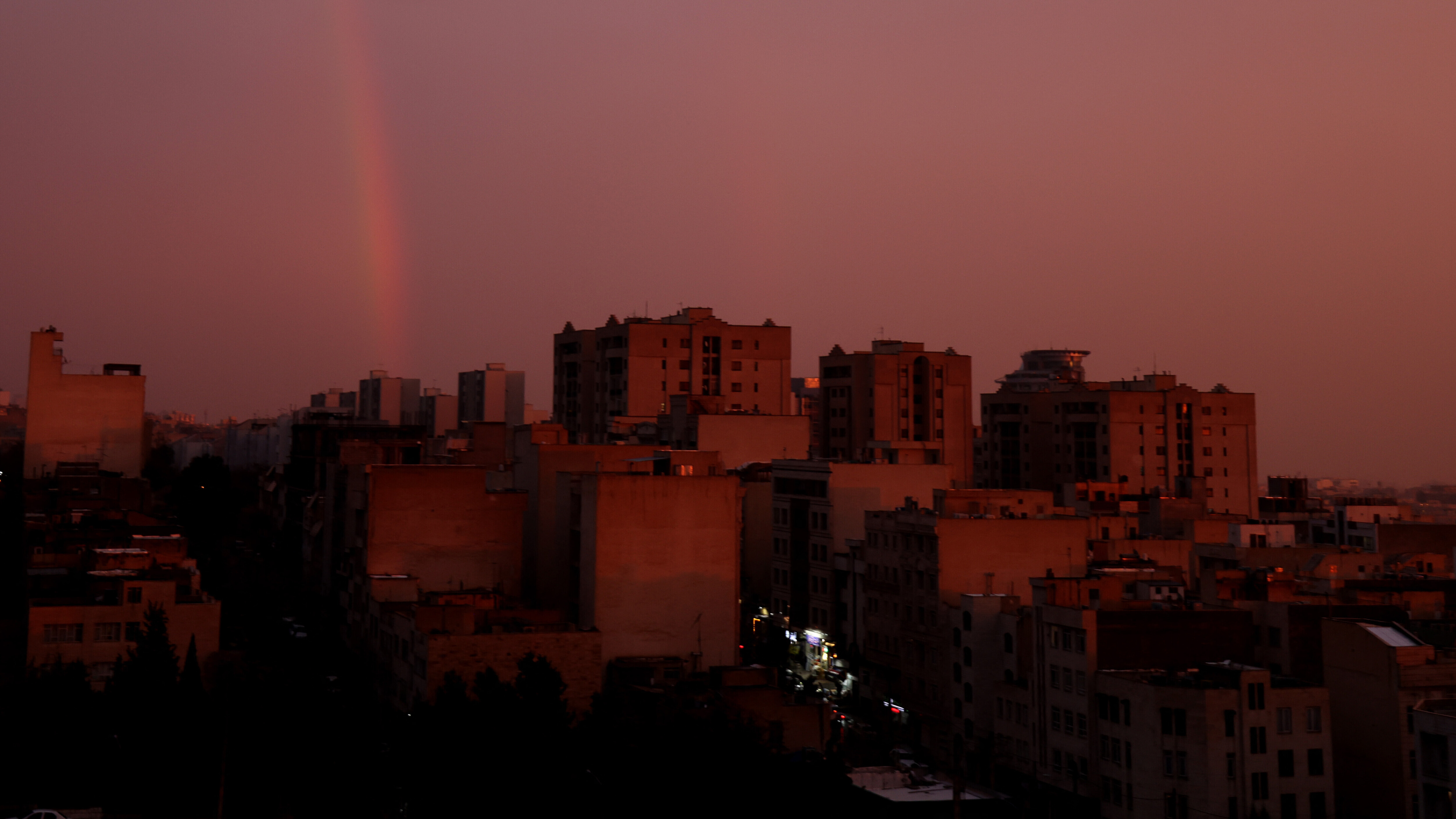 In der iranischen Hauptstadt Teheran geht gerade die Sonne auf. Über den Häusern der Stadt hängt eine dichte, rosafarbene Wolkendecke. Das Bild wurde am 10.12.25 aufgenommen.