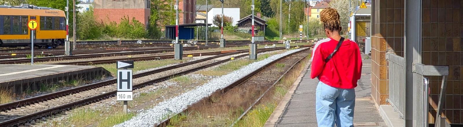 Eine Frau steht auf dem Bahnsteig und  ihre Tasche steht auf den Boden, während sie am Bahnhof Weiden in Bayern auf einen Zug wartet.