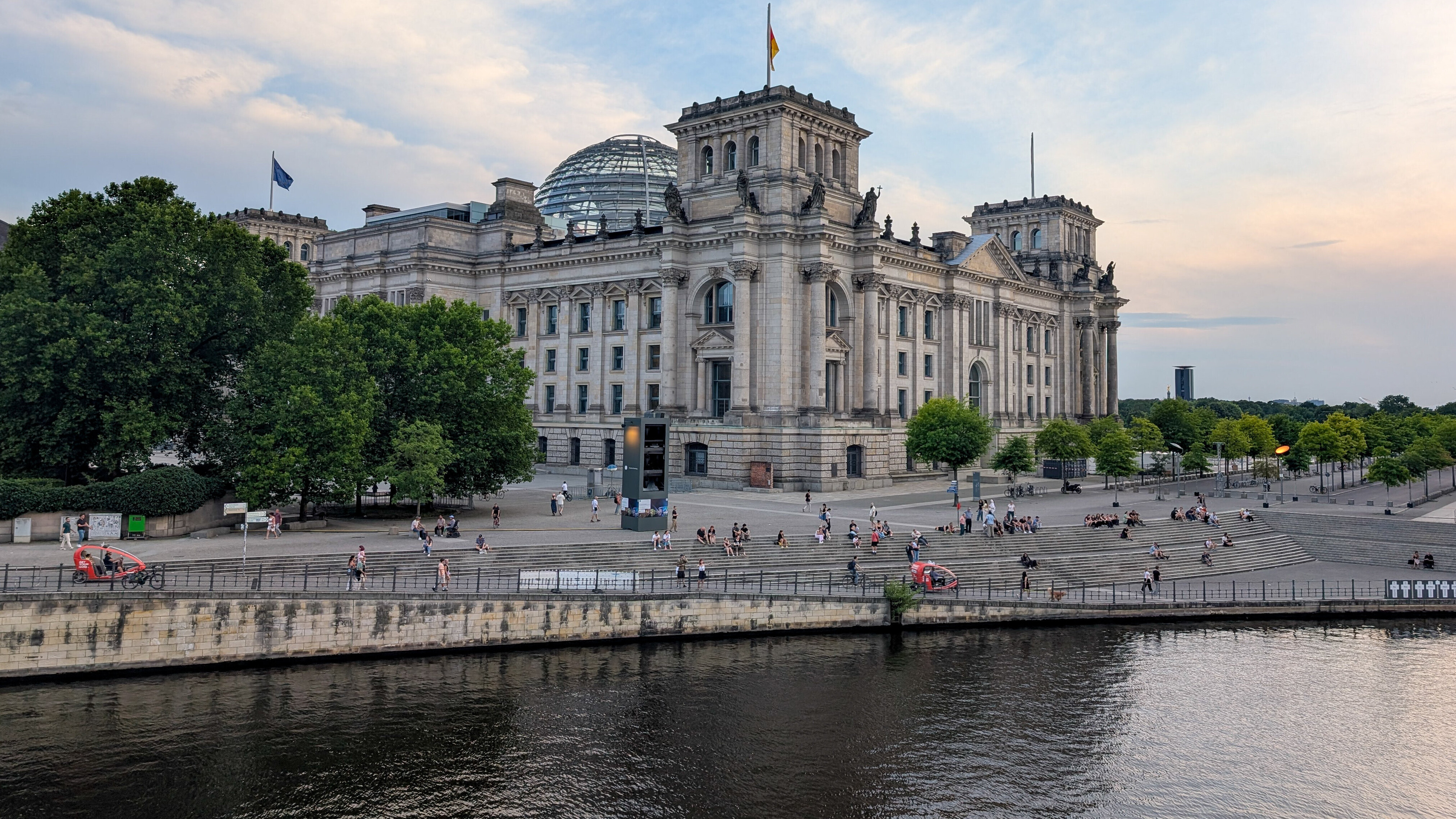 Das Reichstagsgebäude mit der Glaskuppel von der Seite. Davor ist die Spree zu sehen.