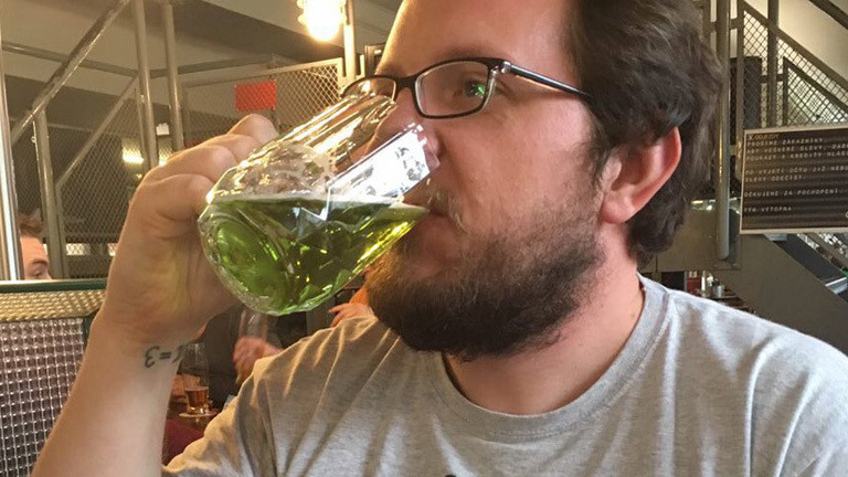 Reinhard Remfort mit Brille und Bart. Er trinkt aus einem großen Bierglas eine grüne Flüssigkeit.