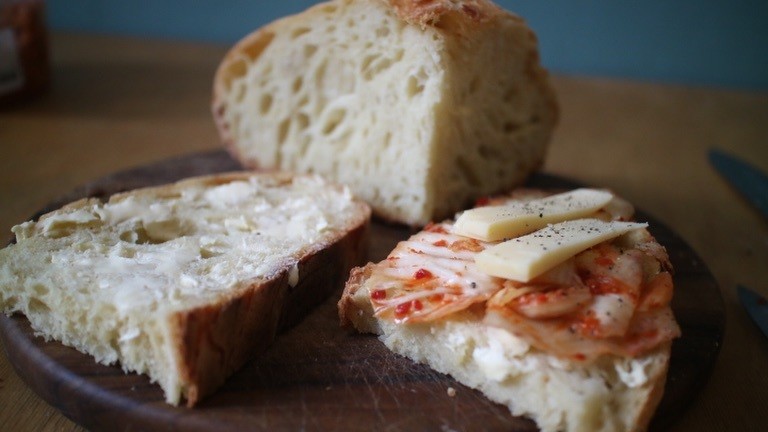 Scheiben selbstgebackenen Sauerteigbrotes bestrichen mit Mutter und belegt mit Kimchi und Käse.
