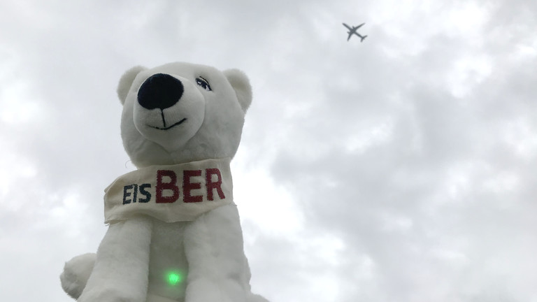 Netzbasteln #151: Ein Stofftier-Eisbär mit Aufschrift "EisBER" vor bewöltem Himmel, im Hintergrund fliegt ein Flugzeug vorbei