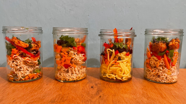 In Schraubgläser werden Mie-Nudeln, Paprika, Möhre, Koriander, Sezuan-Tofu und Frühlingszwiebeln geschichtet.