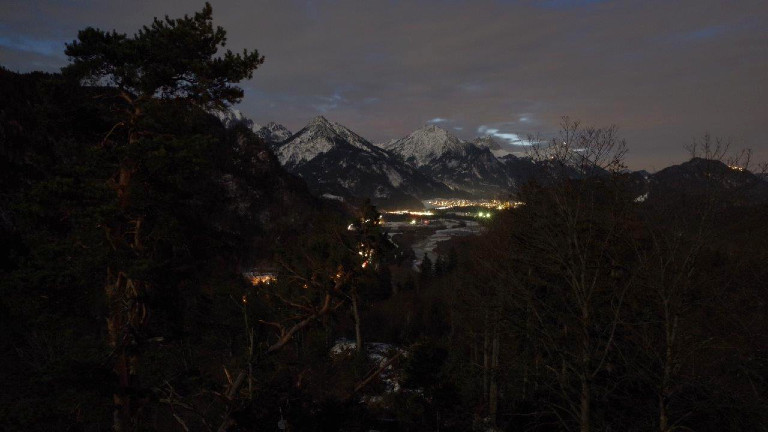 Blick durch die Wälder auf ein beleuchtetes Dorf bei Nacht
