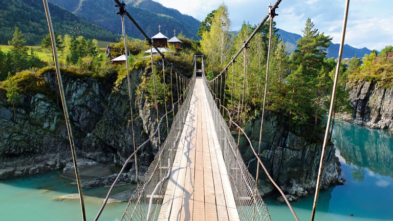Eine Brücke über einem Abhang vor blauem Wasser.