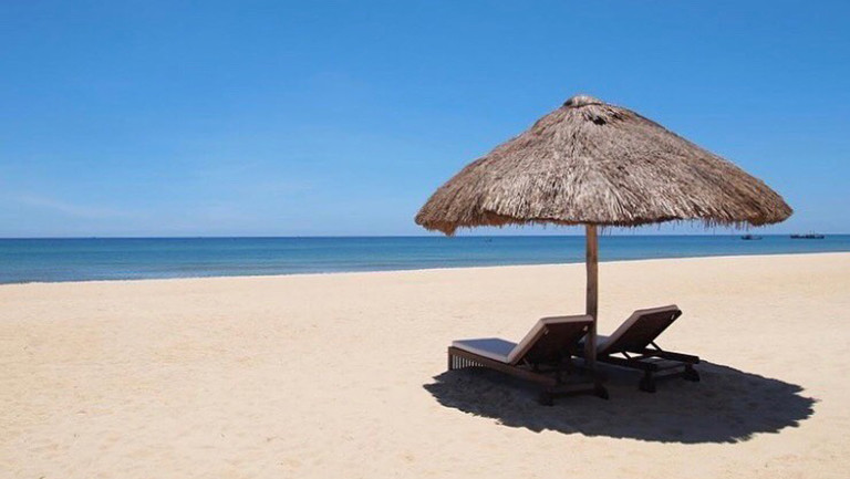 An einem leeren Strand von Zentralvietnam stehen zwei leere Liegen mit Sonnenschirm.