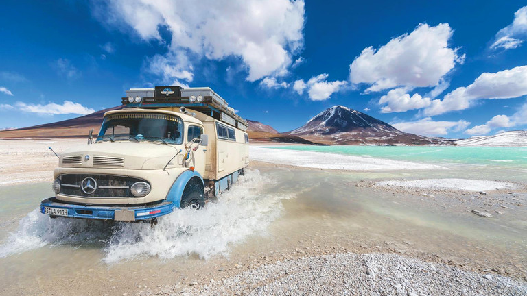 Ein Oldtimer fährt durch eine grüne Lagune in Bolivien.