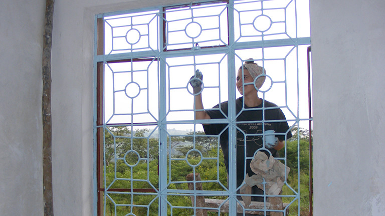 Eine Frau beim Fenster streichen.