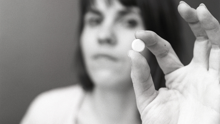 Eine Frau hält eine weiße Pille zwischen ihren Fingern. Eine Illustration für die Einnahme von Medikamenten oder für Antibabypillen zu dieser Zeit. Schweden 1971