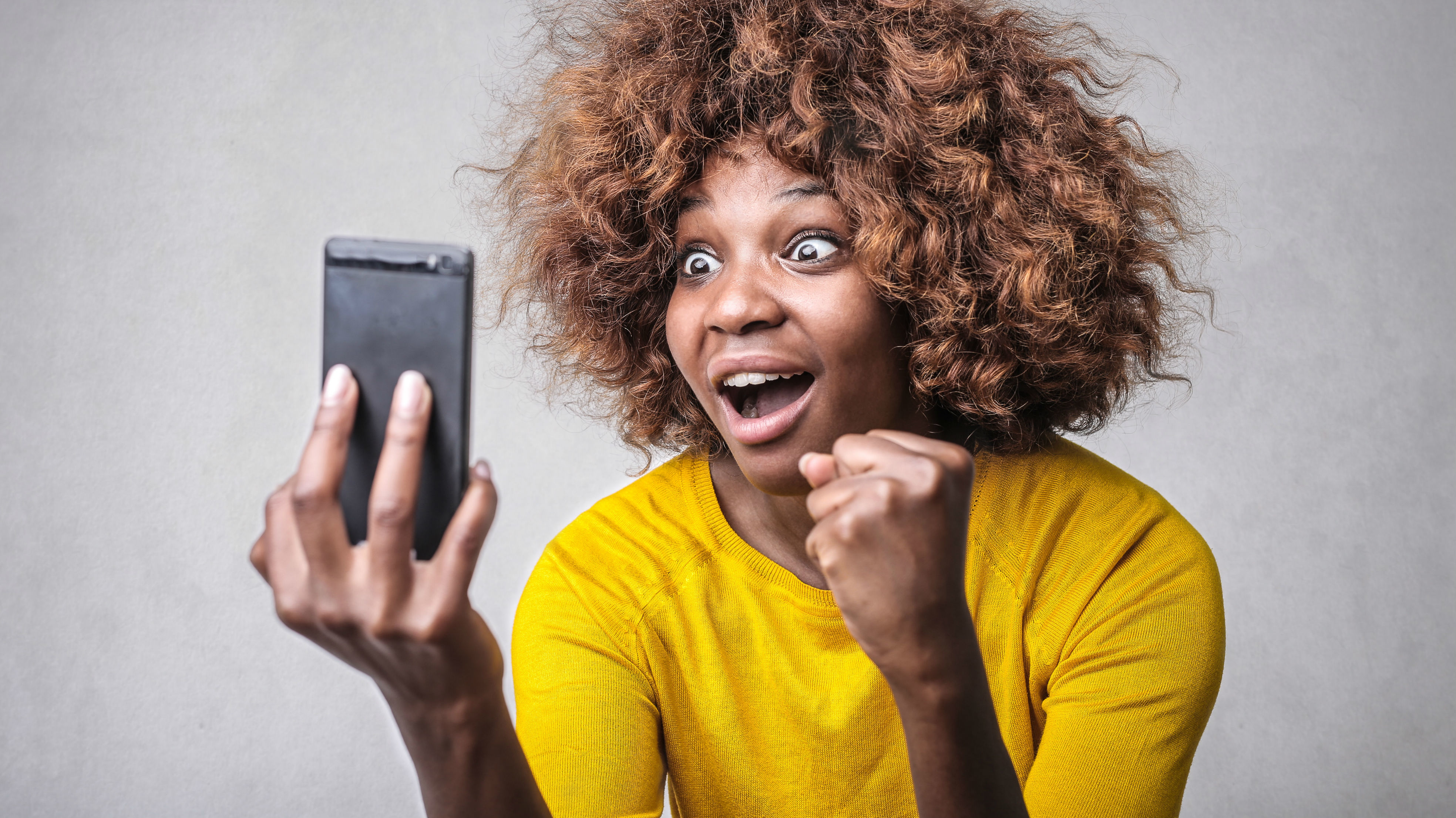 Eine Frau schaut auf ihr Smartphone und freut sich.