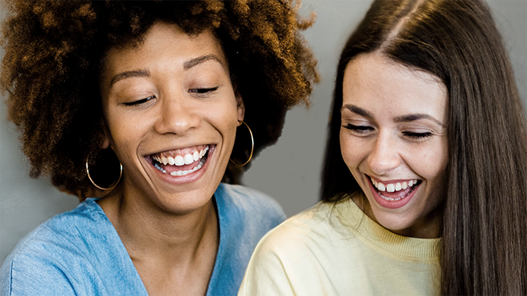Zwei junge Frauen betrachten lachend einen Bildschirm.