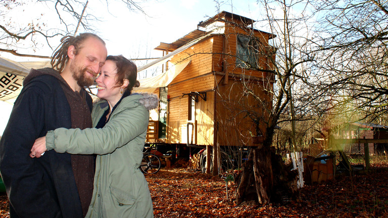 Nicole und Cartsen Dau umarmen sich, im Hintergrund ihr 25 Quadratmeter großes Haus.