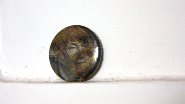 Ein Button des Künstlers Ruppe Koselleck, gemacht aus einem Ein-Dollar-Schein und Rohöl.