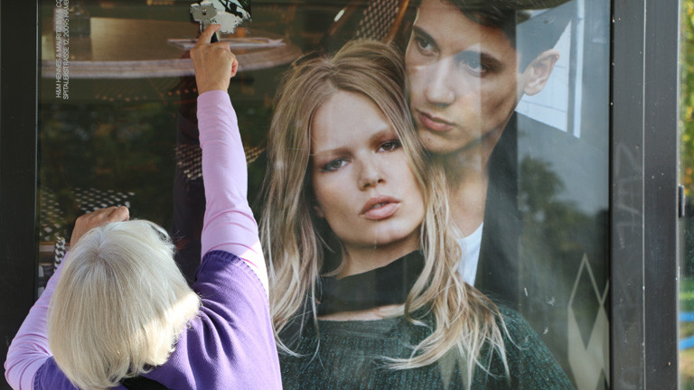 Irmela Mensah-Schramm kratzt einen Aufkleber von einer Plakatwand.