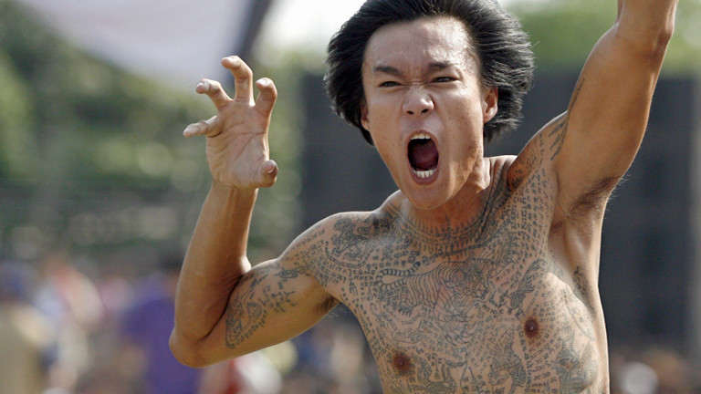 Ein tätowierter Mann auf dem Wai-Kru-Tattoo-Festival in Wat Bang Phra macht gefährliche Grimassen und Gesten.