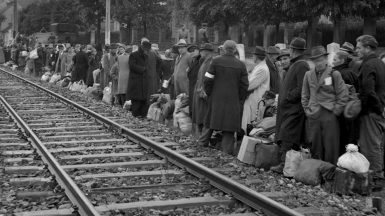Deutsche Vertriebene stehen an einem Gleis und warten auf ihren Abtransport.