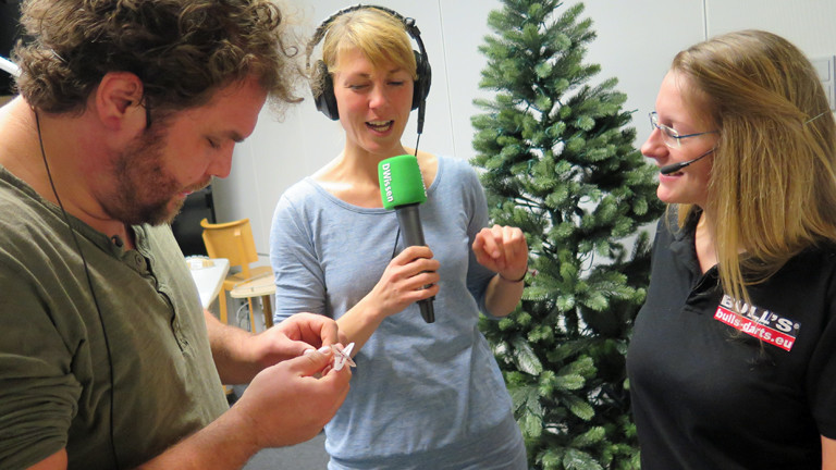 DRadio-Wissen-Moderatoren Paulus Müller und Nora Hespers lassen sich von Dart-Jugendmeisterin Ann-Kathrin Wigmann ihren Sport zeigen.