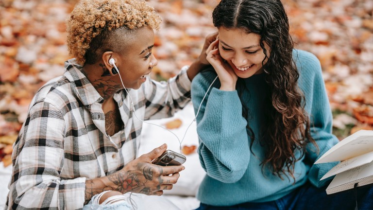Zwei Frauen teilen sich einen Kopfhörer und spielen etwas von ihrem Smartphone ab.