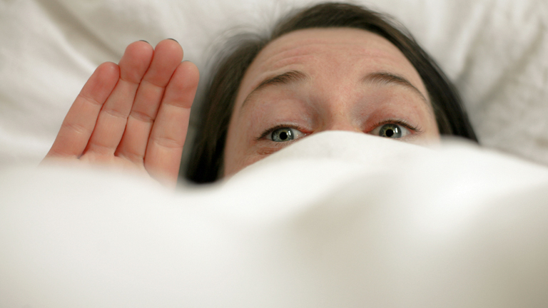 Eine Frau schaut kränkelnd über die Bettdecke hinaus.