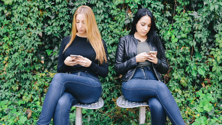 Zwei Frauen sitzen nebeneinander und tippen auf ihren Smartphones herum.
