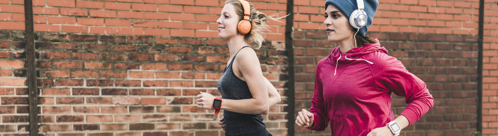 Zwei Mädels joggen mit Fitnessarmband und Kopfhörern.