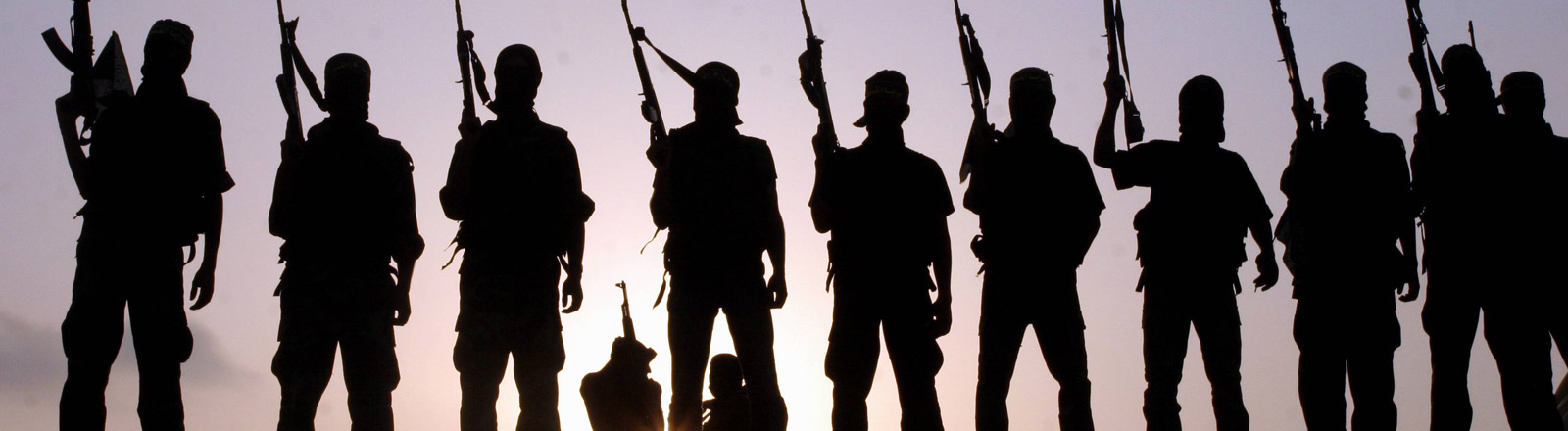 Kämpfer des Islamischen Staates stehen in einer Reihe und halten Waffen nach oben
