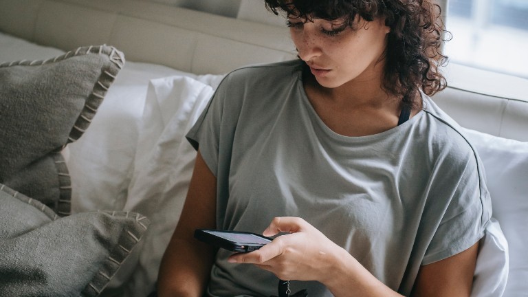 Eine Frau sitzt auf ihrem Bett und scrollt auf ihrem Handy.