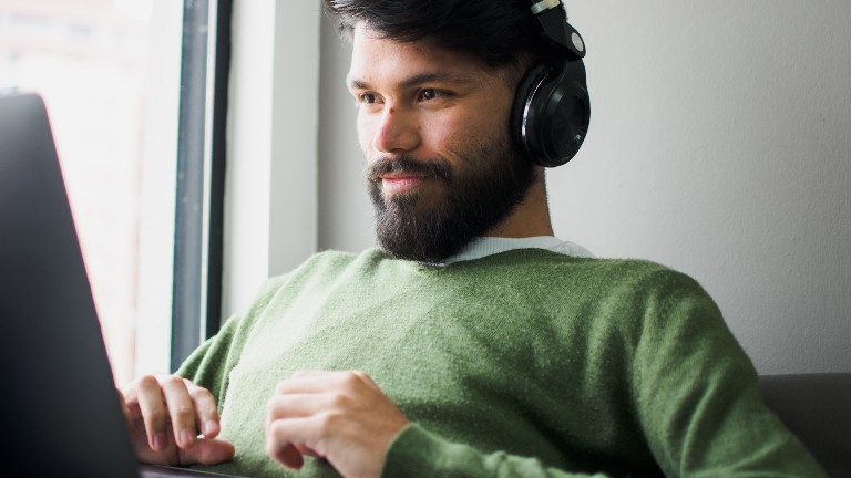 Ein Mann mit Kopfhörern auf den Ohren sitzt an einem Computer.