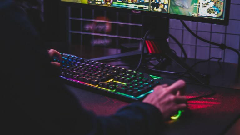 Eine Person sitzt an einer bunt leuchtenden Computertastatur und spielt ein Videospiel.