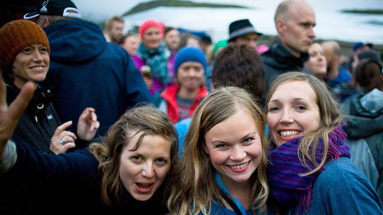 Drei Frauen lachen in die Kamera, sie sind umgeben von Menschen.