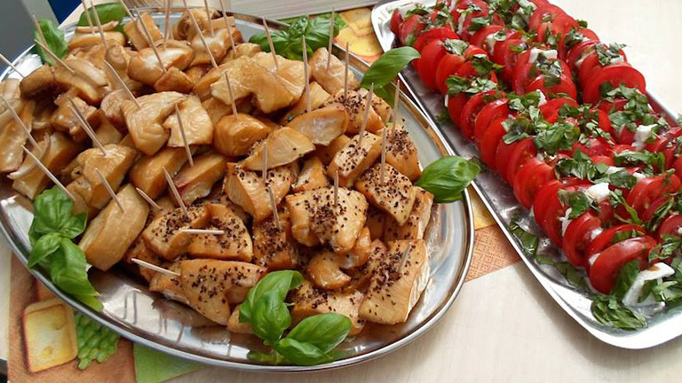 Zwei silberne Platten: Auf der einen liegen Fischstücke, auf der anderen Tomaten mit Mozzarella.