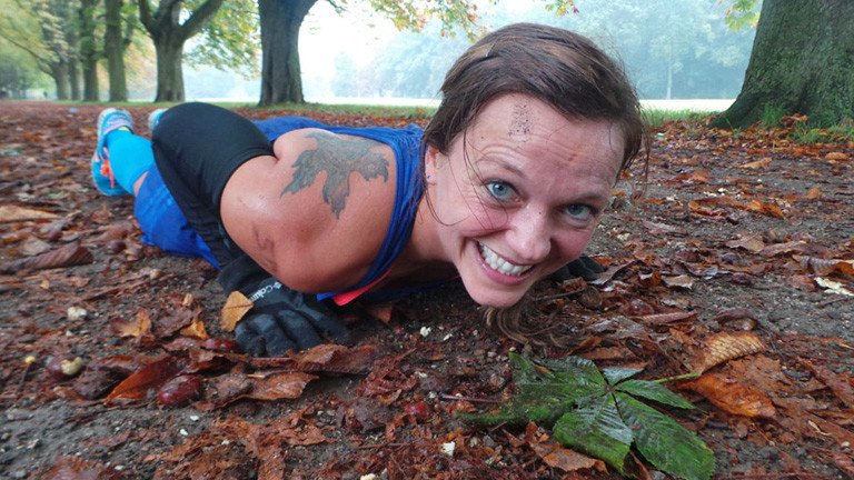 Anita Horn macht eine Liegestütze auf einem Waldweg voll mit Laub. Sie lächelt angestrengt in die Kamera.