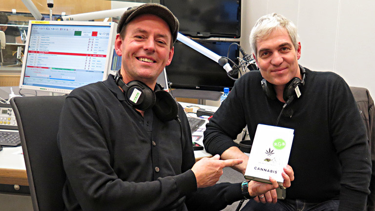 Rainer Schmidt und Moderator Manuel Unger sitzen im Studio. Unger hält das Buch von Schmidt und zeigt darauf.