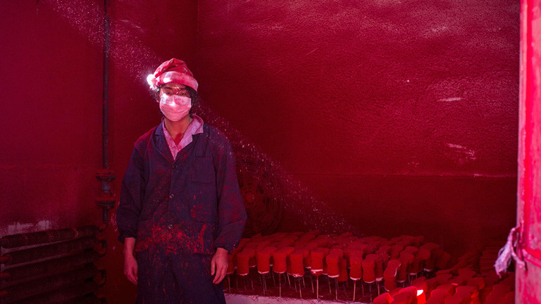 Ein Arbeiter steht mit Weihnachtsmütze bekleidet in einem Raum, der rot von Farbspritzern ist. Hinter ihm stehen aufgereiht zum Trocknen rote Weihnachtsmännerschuhe; Bild: dpa