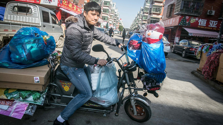 In der chinesischen Stadt Yiwu sitzt ein junger Mann auf einem Moped, das mit Weihnachtsdeko bepackt ist; Bild: dpa