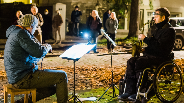 Ein Geiger und ein Saxophonist musizieren auf einem Grünstreifen.