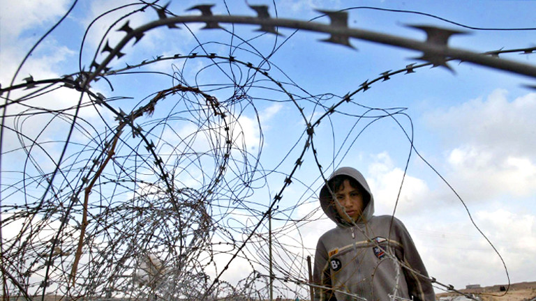 Ein Junge in einem Geflecht aus Natodrähten. Aufgenommen im Sperrgebiet des Gazastreifens 2006.