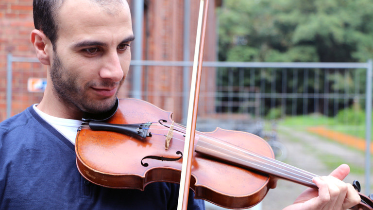 Omar spielt auf einer Geige im Heim in Brandenburg