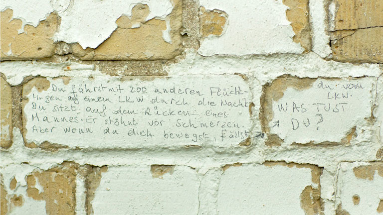 Rissige Wand mit einer darauf gekritzelten Geschichte einer Flucht.