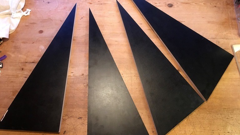 Schwarze dreieckige Multiplex-Platten liegen auf einem Holzfußboden.