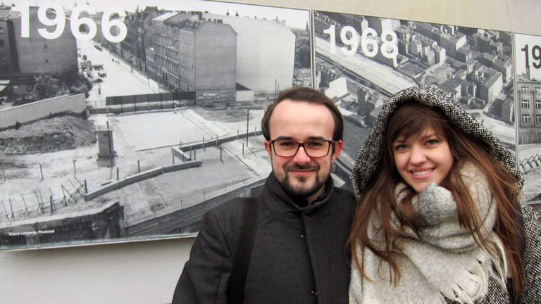 Anna und Sebastian aus Polen stehen vor Schwarz-Weiß-Bildern mit der Berliner Mauer.