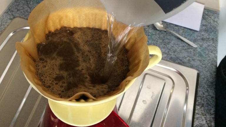 Heißes Wasser wird auf Kaffeepulver aufgegossen.