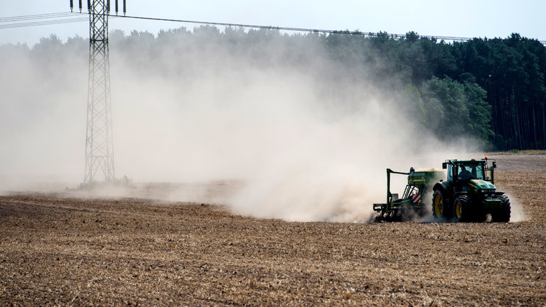 Ein Traktor fährt über ein trockenes Feld und wirbelt Staub auf