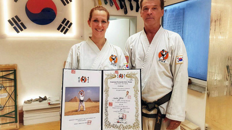 Caro steht mit einer Urkunde in der Hand neben ihrem Taekwondolehrer.