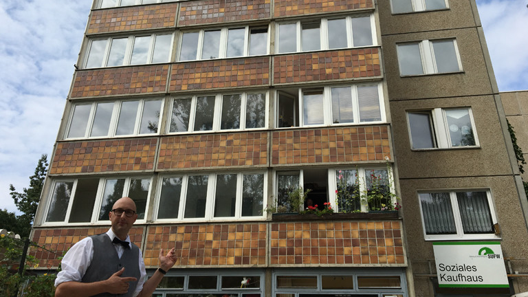 Front eines Plattenbaus mit Mann davor