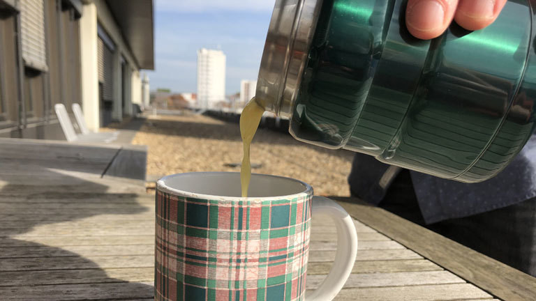 Ein weihnachtlicher Becher, in den ein Heißgetränk aus einer Thermoskanne eingegossen wird.