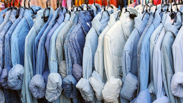 Viele Jeanshemden hängen hintereinander an einer Stange.