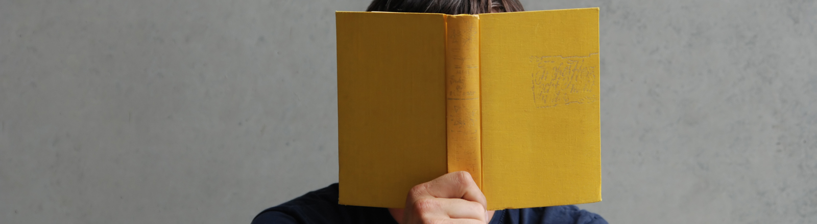 Mann hält sich ein Buch vor das Gesicht